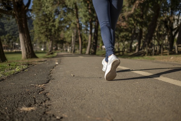 Back, bottom half of a girl in jeans and white trainers running along a forest road